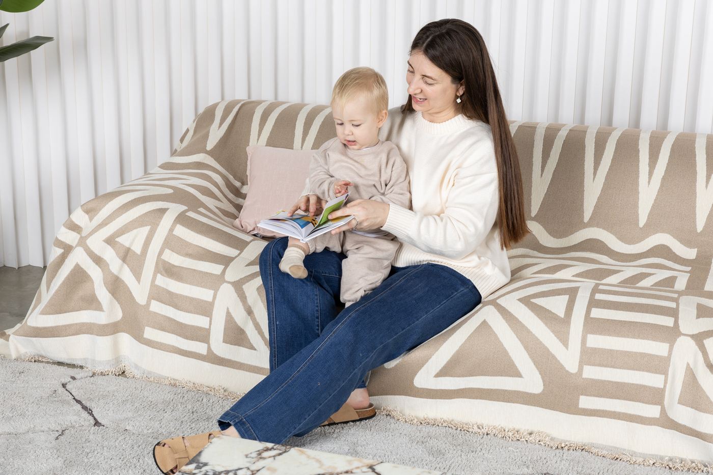 Woman and toddler reading on a sofa with a cream patterned CouchCare cover.